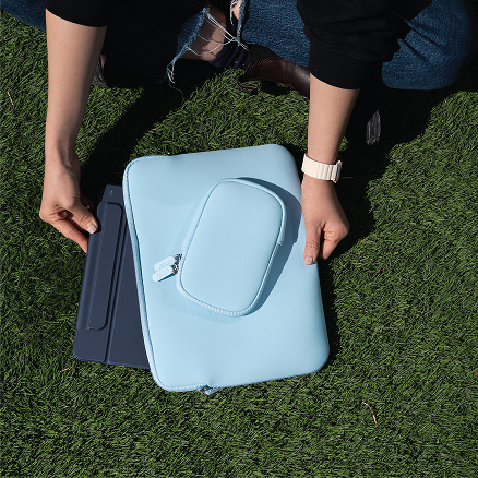 Person placing a tablet and sleeve into a backpack on grass.